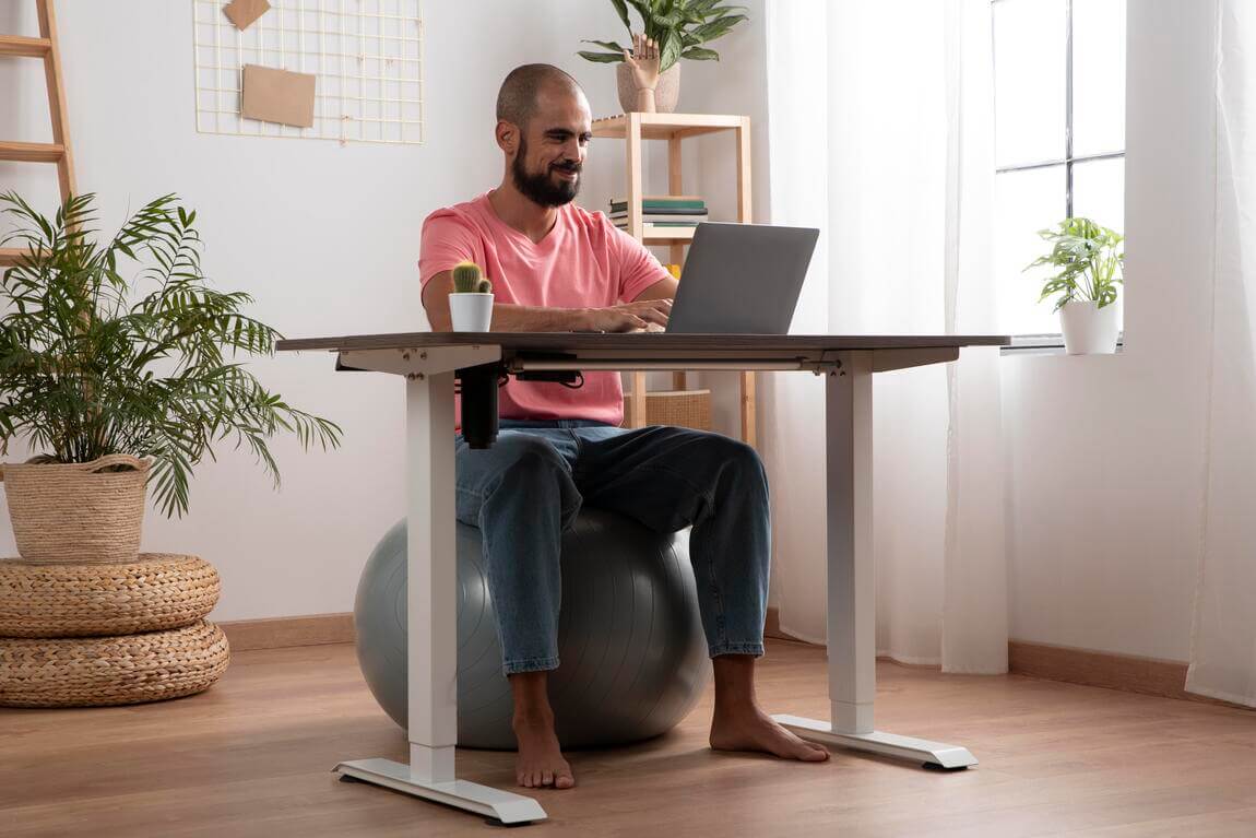 hombre sentado en una pelota  de yoga, trabajando frente a un escritorio ergonomico