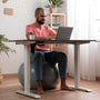 hombre sentado en una pelota  de yoga, trabajando frente a un escritorio ergonomico
