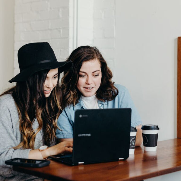 Dos mujeres frente a un computador, en un escritorio y con una taza de café - imagen de la nota de blog de Como mejorar el ambiente laboral