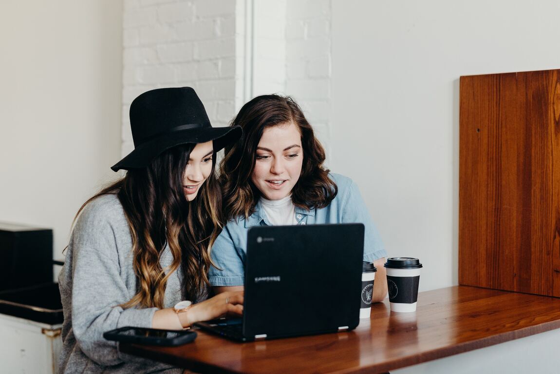 Dos mujeres frente a un computador, en un escritorio y con una taza de café - imagen de la nota de blog de Como mejorar el ambiente laboral