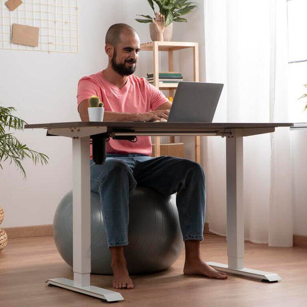 hombre sentado en una pelota  de yoga, trabajando frente a un escritorio ergonomico